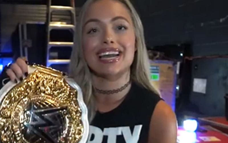 a woman is holding a wrestling championship belt and smiling