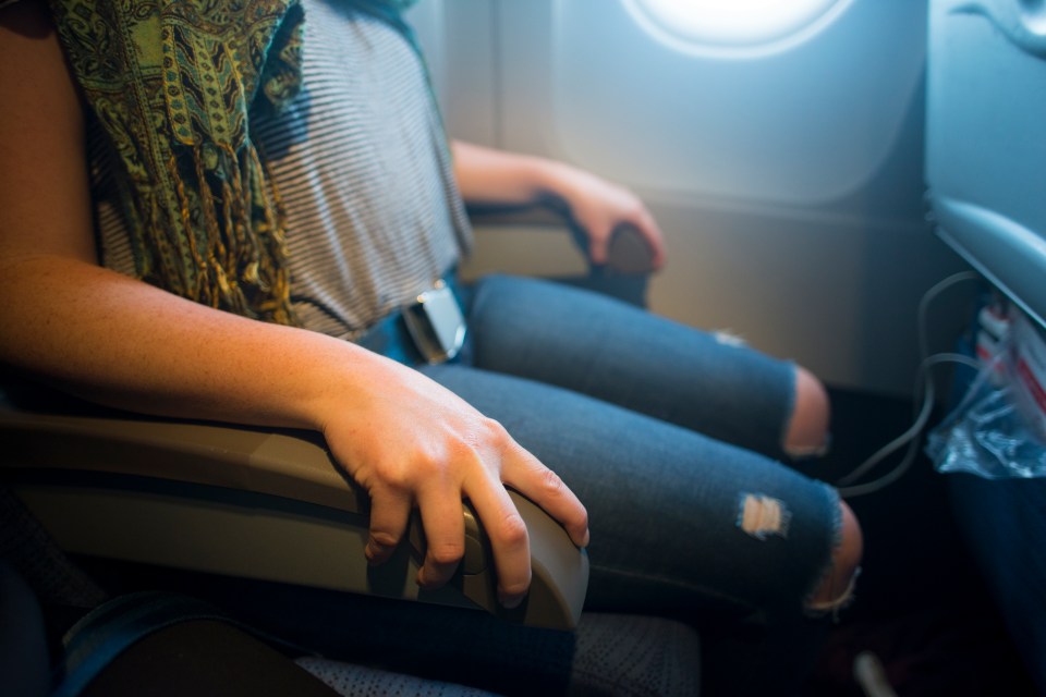 a woman sits on an airplane with her arm resting on the arm rest