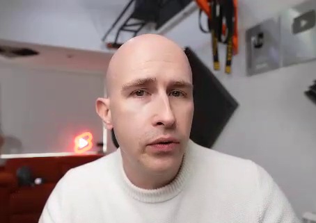 a bald man is wearing a white sweater and looking at the camera .