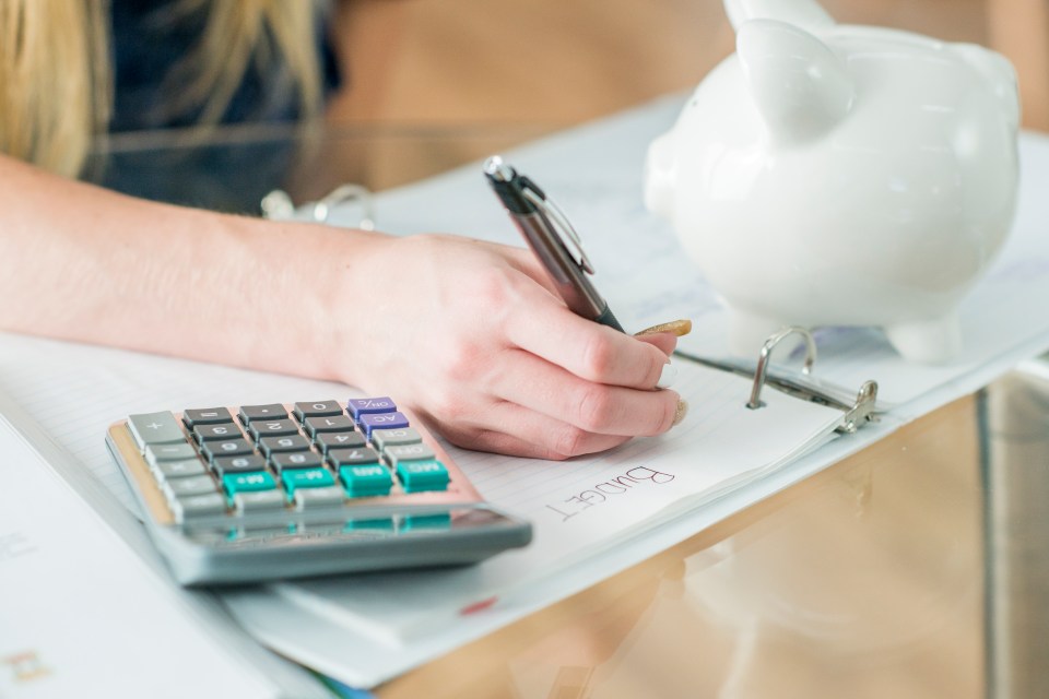 A Caucasian teenage girl is indoors. She is wearing casual clothing. She is writing in her binder. A calculator is on the table.