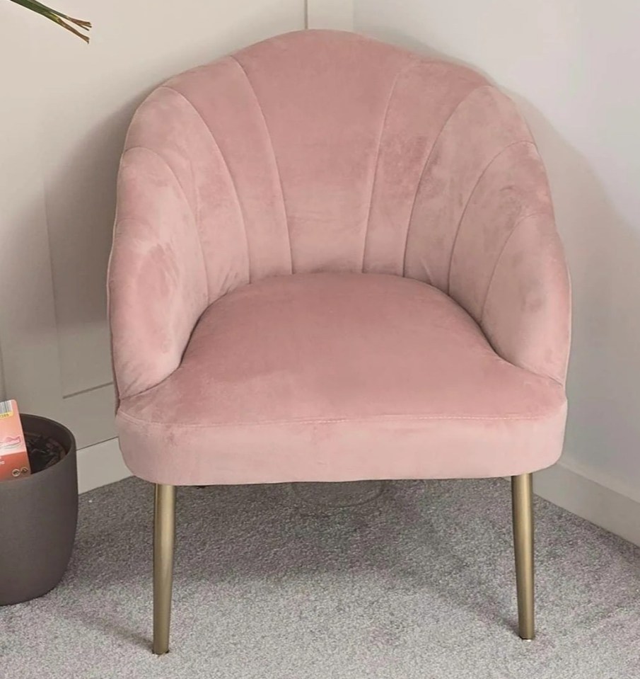 a pink chair with gold legs sits in a corner of a room