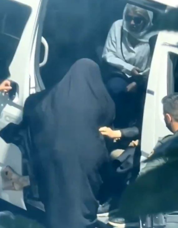 a woman in a hijab is being escorted out of a van