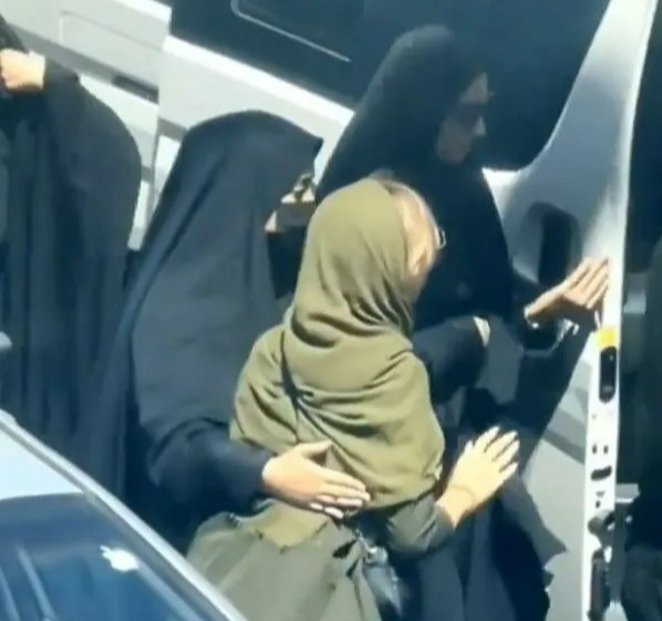 a woman in a hijab is hugging another woman in a car