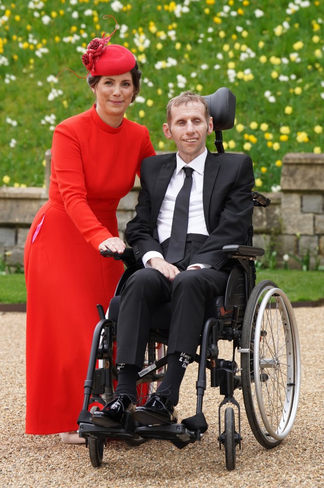 a woman in a red dress stands next to a man in a wheelchair