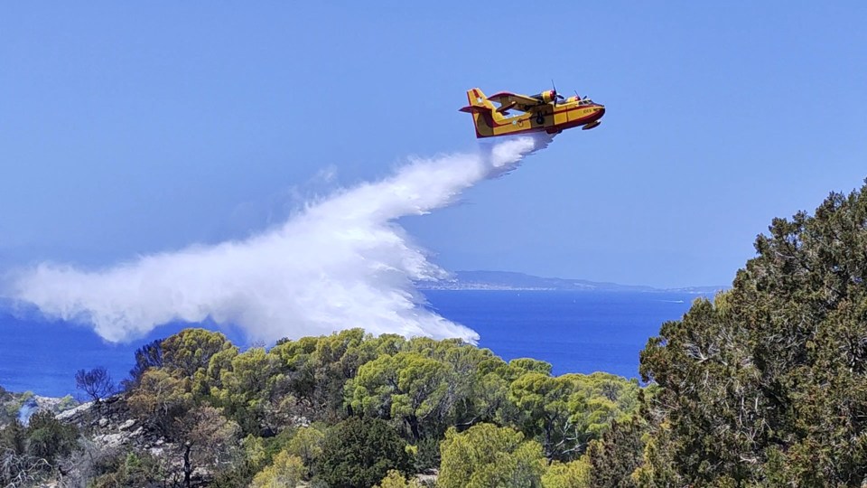 A firefighting plane drops water over an area affected by a forest fire in Hydra