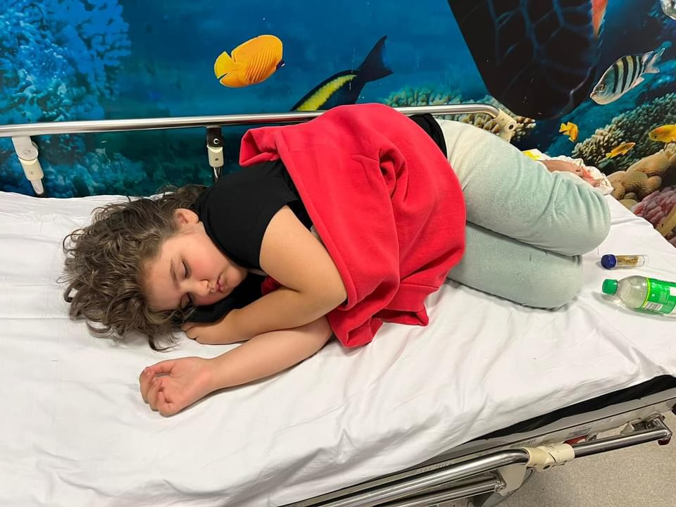 Eight-year-old Amelia lying on a hospital bed after falling ill