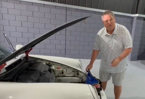 a man is standing next to a white car with the hood open .