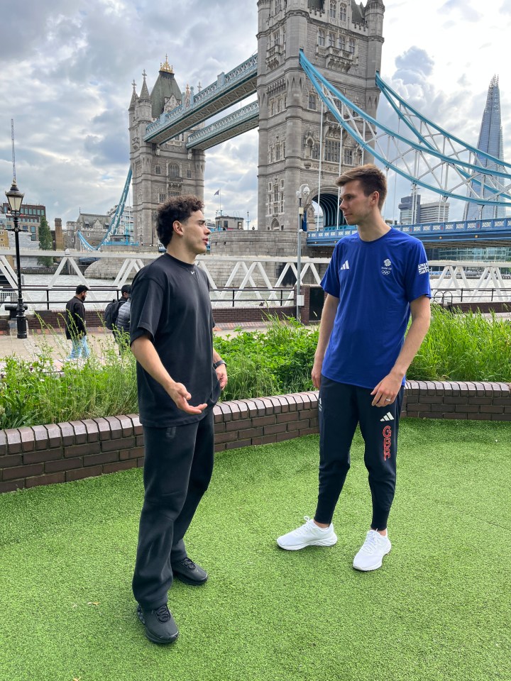 two men standing in front of a bridge with one wearing an adidas shirt