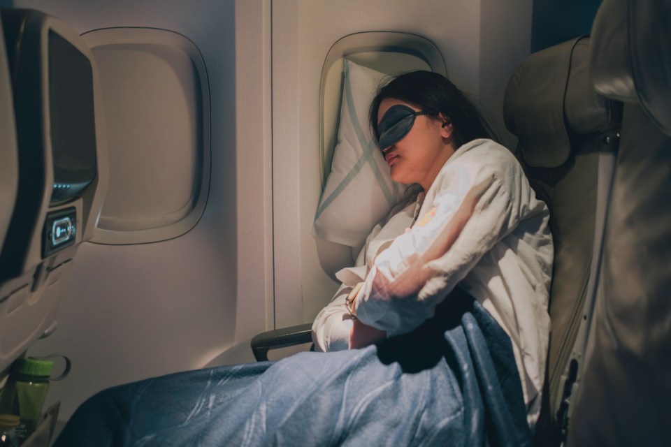 a woman wearing an eye mask is sleeping on an airplane