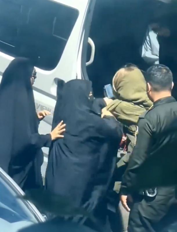 a woman in a hijab is being escorted out of a van