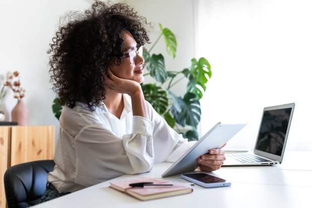 a woman sits at a desk with a tablet and a laptop