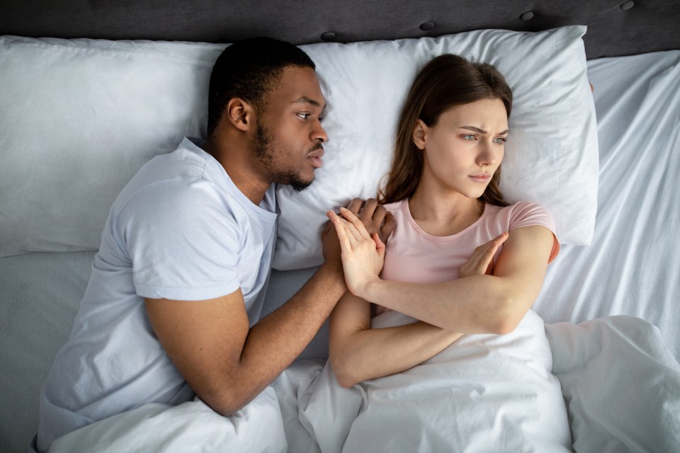 a woman laying in bed with her arms crossed while a man tries to comfort her