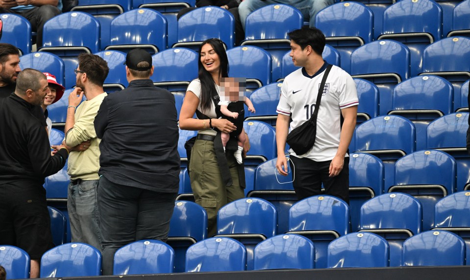 a woman holding a baby talks to a man in an england jersey