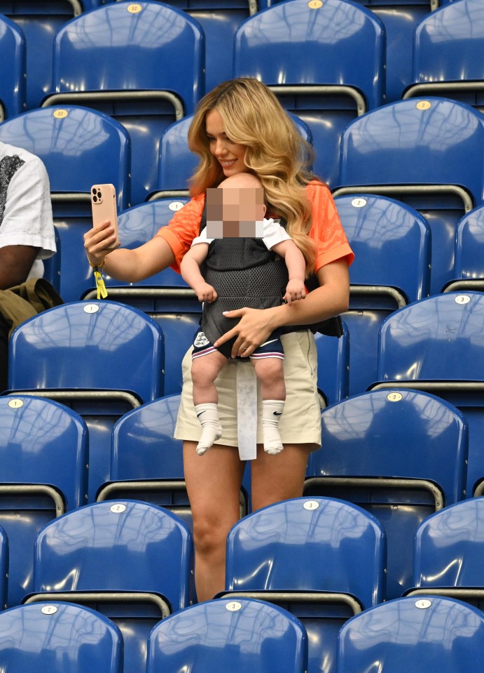 a woman is holding a baby in a carrier and taking a selfie