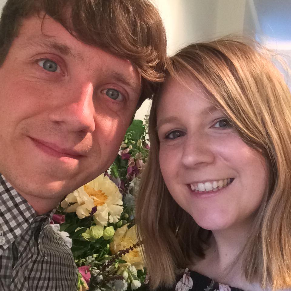 a man and a woman are posing for a picture with flowers in the background