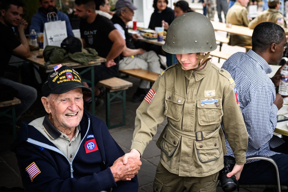 US paratrooper veteran George Cross, 99, poses with a child wearing WWII military attire in Sainte-Mer-l’Eglise, northwestern France