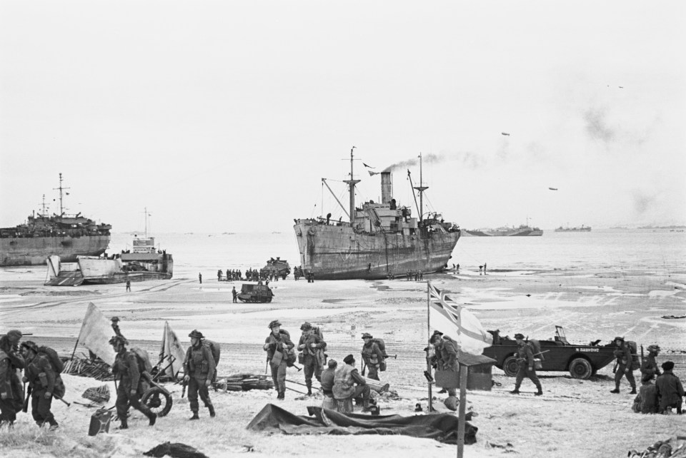 British troops fly the White Ensign of a Naval beach party as they move inland from landing craft