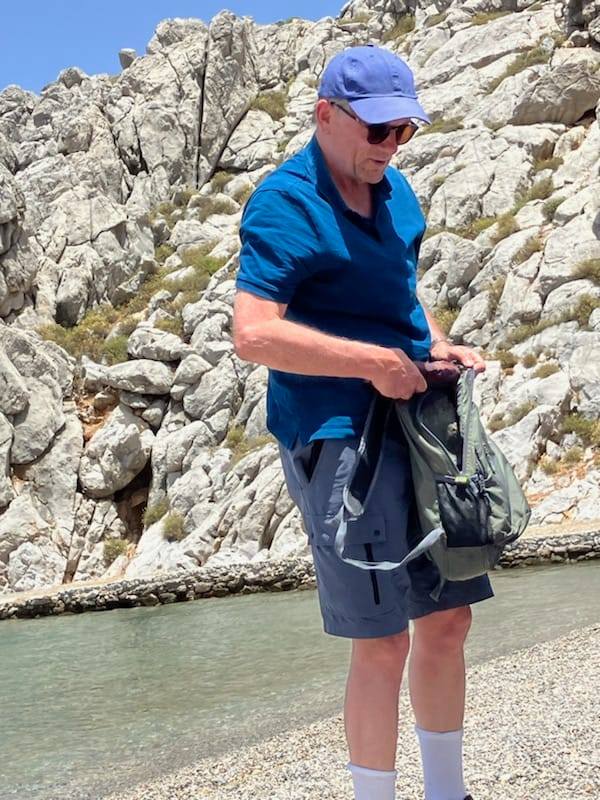 a man wearing sunglasses and a blue hat holds a backpack