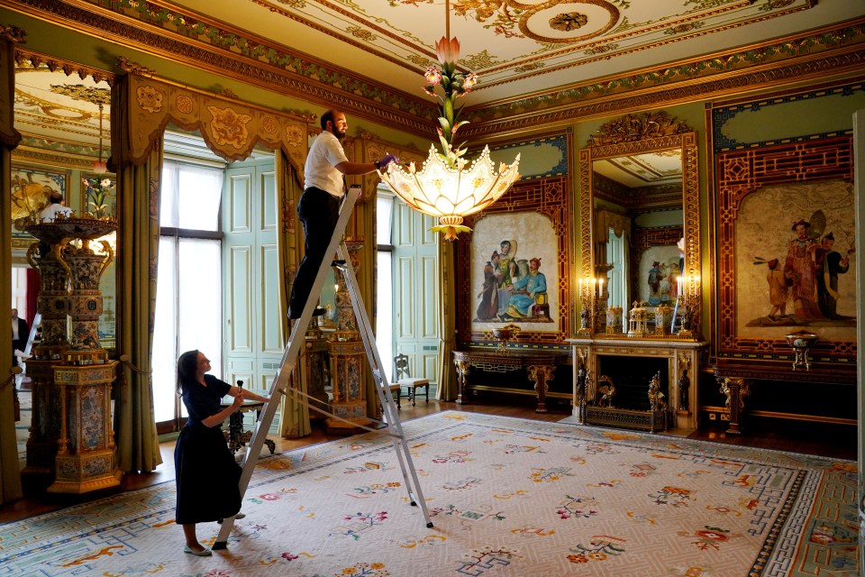 Final preparations are made in the East Wing's Centre Room, where members of Royal Collection Trust staff tend to a chandelier