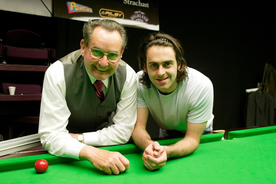 two men standing next to a pool table with a sign that says strachan on it