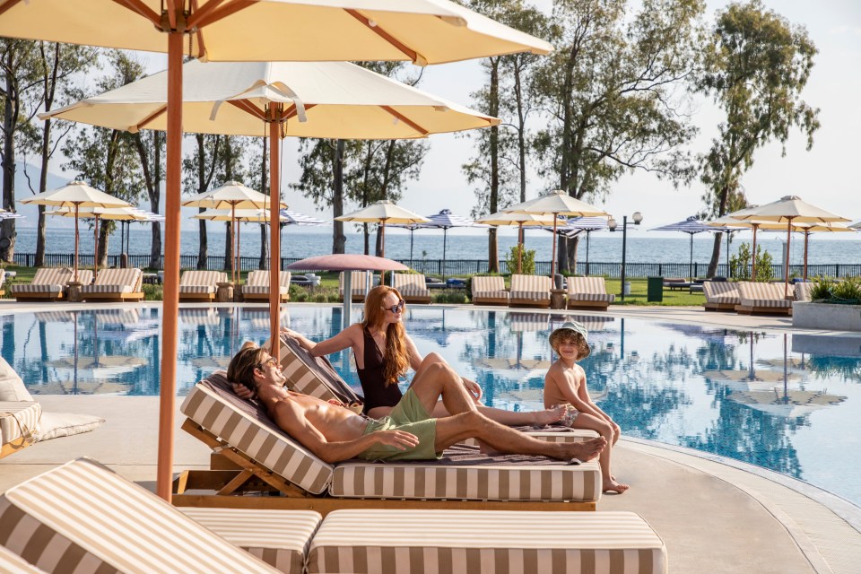 a family sits on lounge chairs near a swimming pool