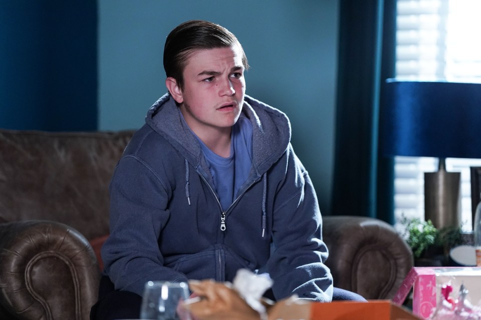 a young man in a grey hoodie sits on a couch