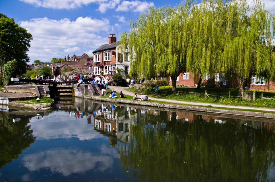 a group of people sit on the side of a river in front of a building that says ' the crown ' on it