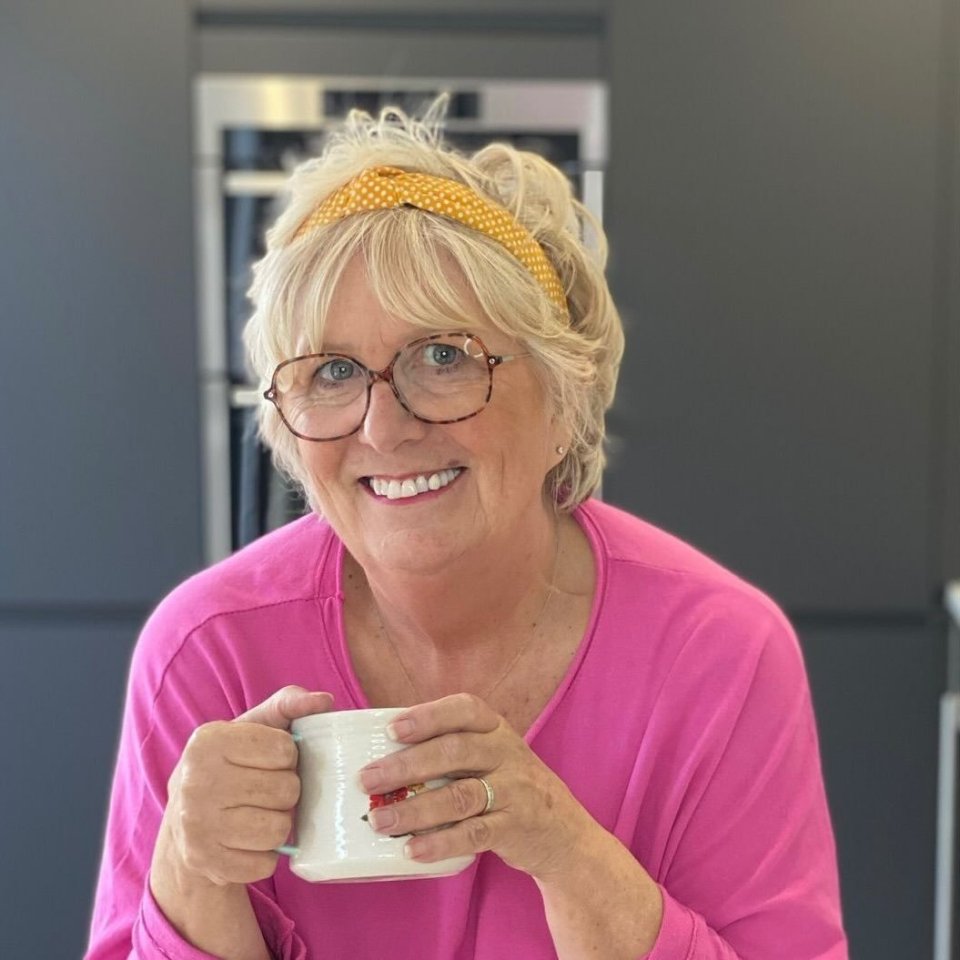 a woman wearing glasses and a pink shirt is holding a cup of coffee