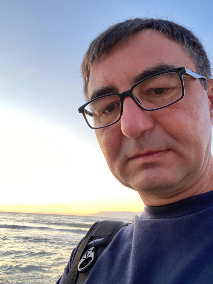 a man wearing glasses stands in front of the ocean