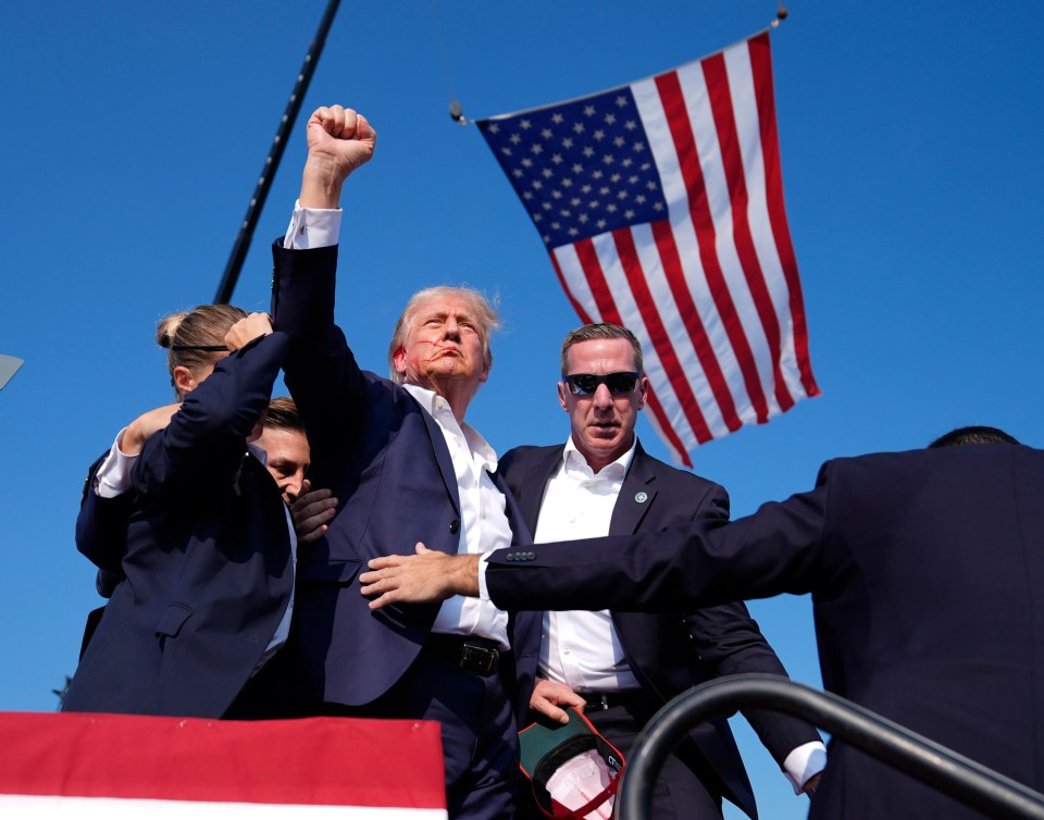 a man in a suit holds up his fist in front of an american flag