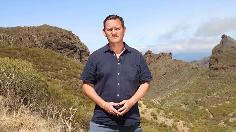 a man in a blue shirt stands in front of a mountain range