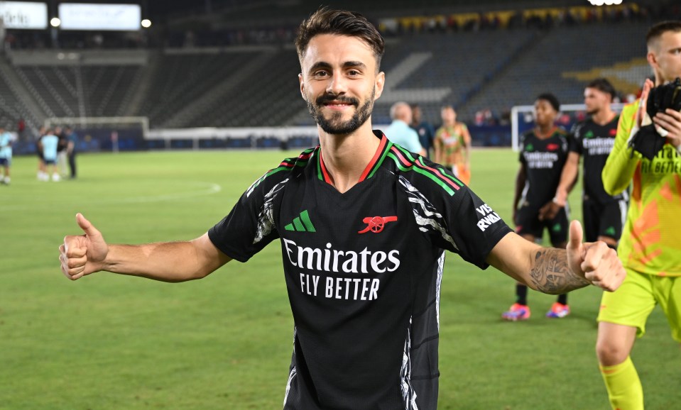 a soccer player wearing an emirates fly better jersey gives a thumbs up