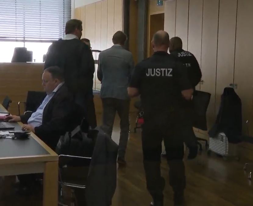 a man in a suit sits at a desk in front of a justiz officer