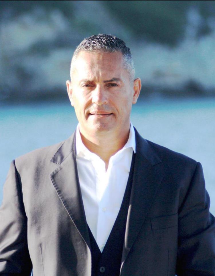 a man in a suit and white shirt stands in front of a body of water