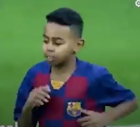 a young boy wearing a barcelona jersey is standing on a soccer field .