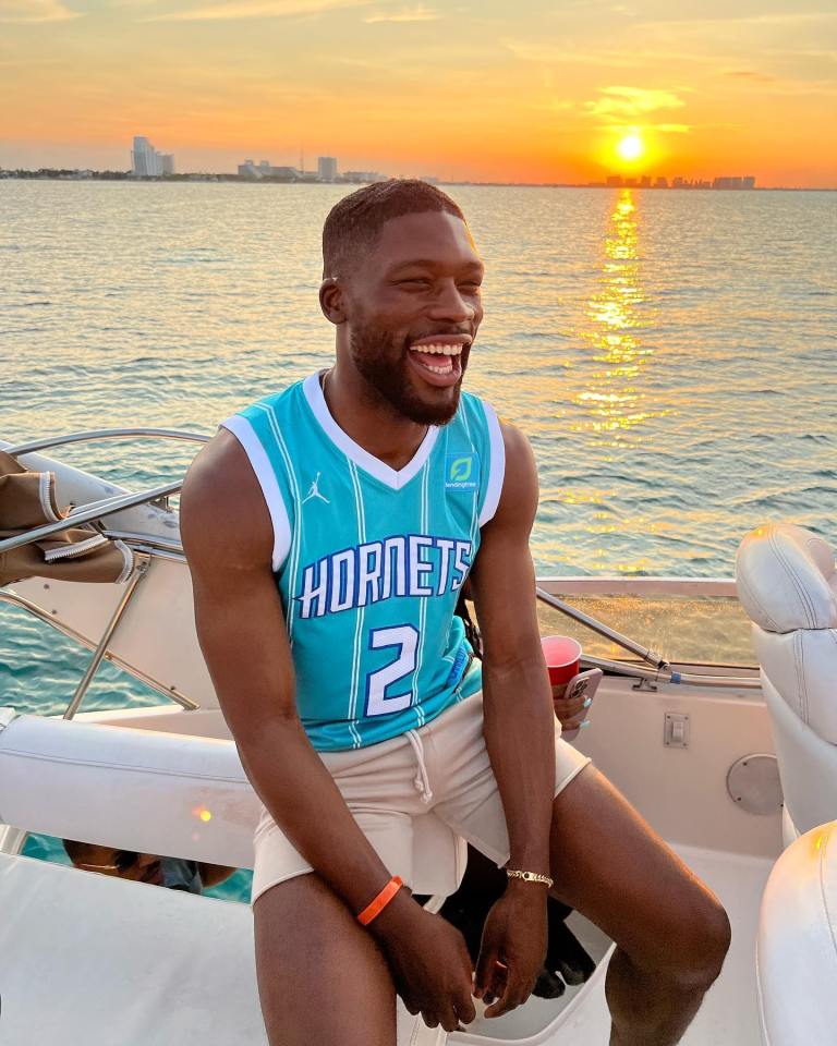 a man wearing a hornets jersey sits on a boat