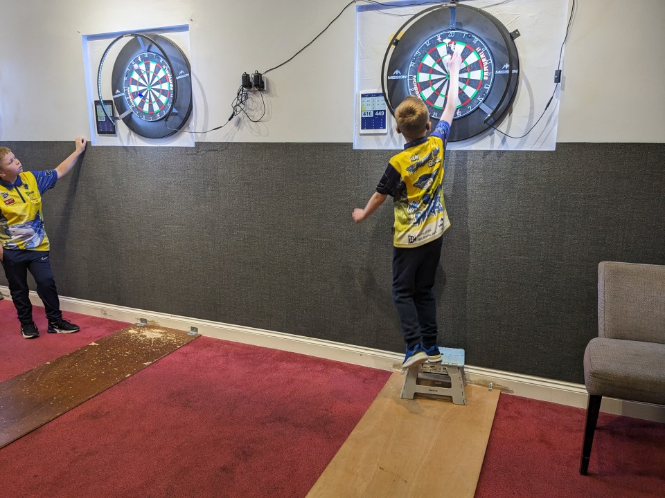 two boys are playing darts and one has a shirt that says ' sharks ' on it