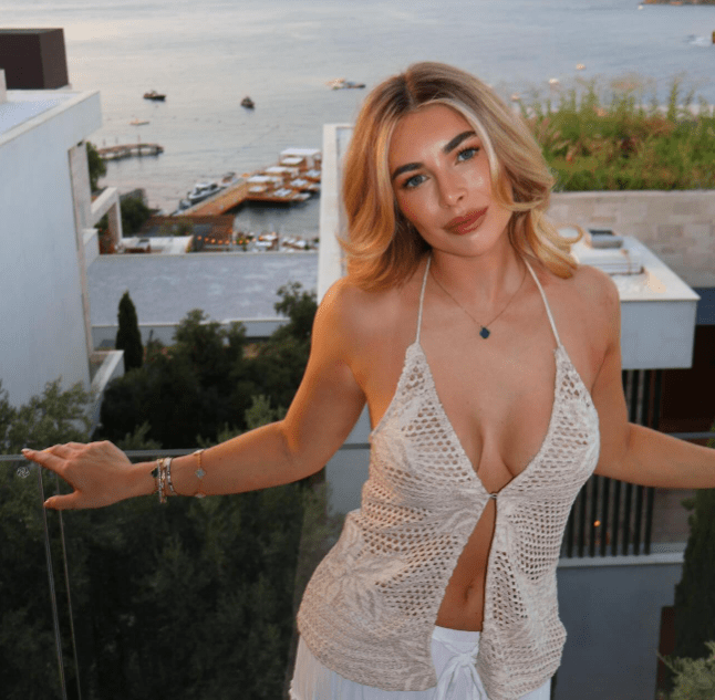 a woman in a halter top stands on a balcony overlooking the ocean