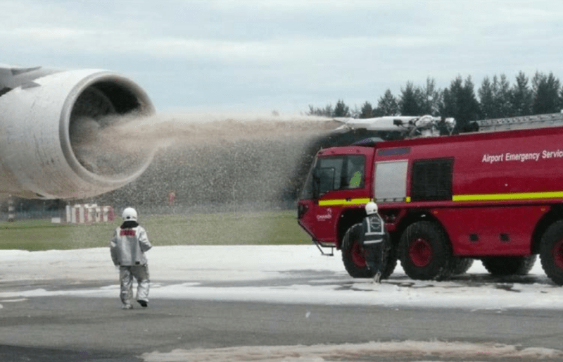 a red airport emergency service truck is spraying foam