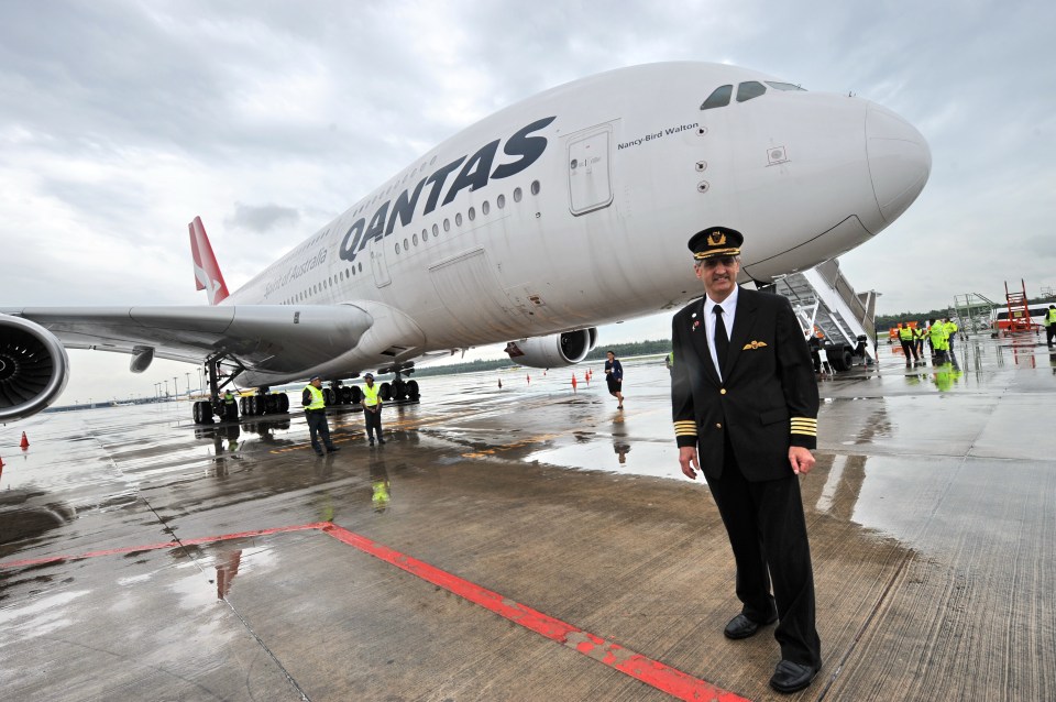 a pilot stands in front of a qantas plane