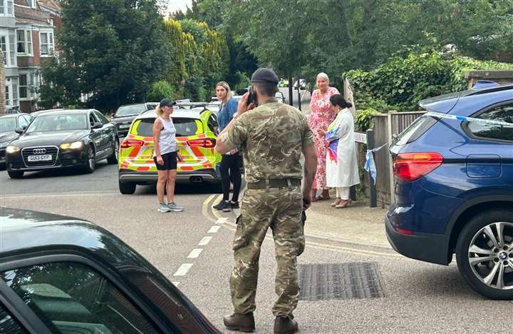 A soldier stands by a group of locals with a police car nearby