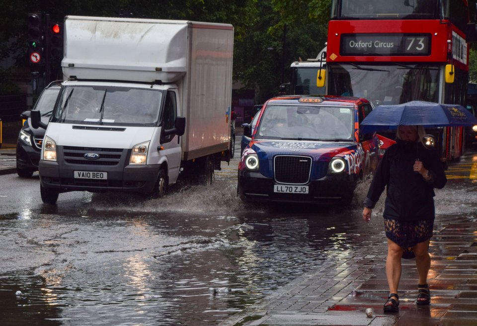 Cars splash through a large puddle on Euston Road as heavy rain drenches the capital