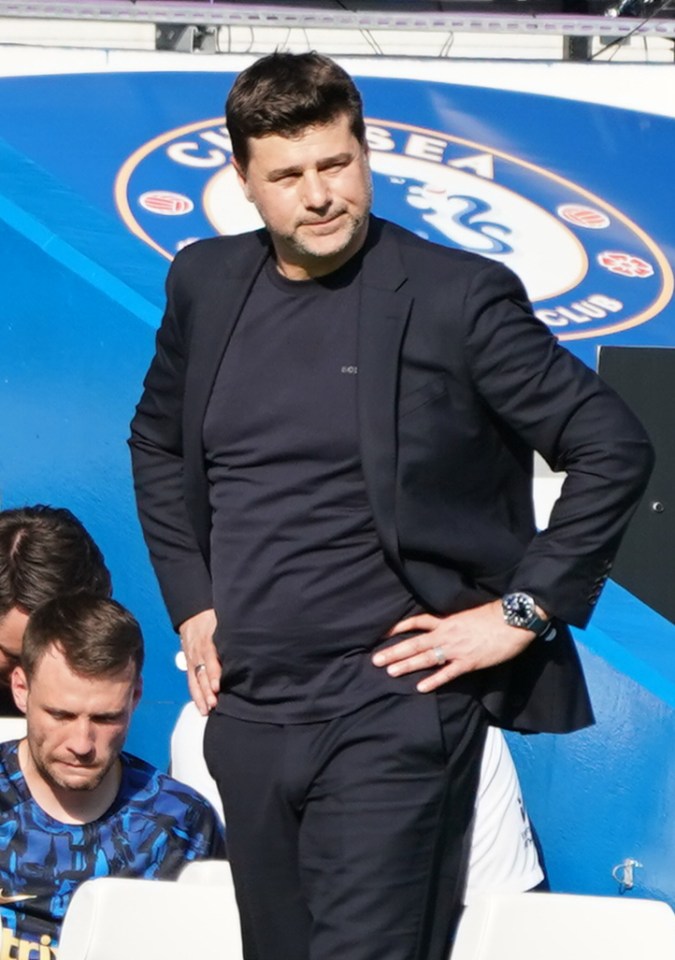 a man in a suit stands in front of a chelsea logo