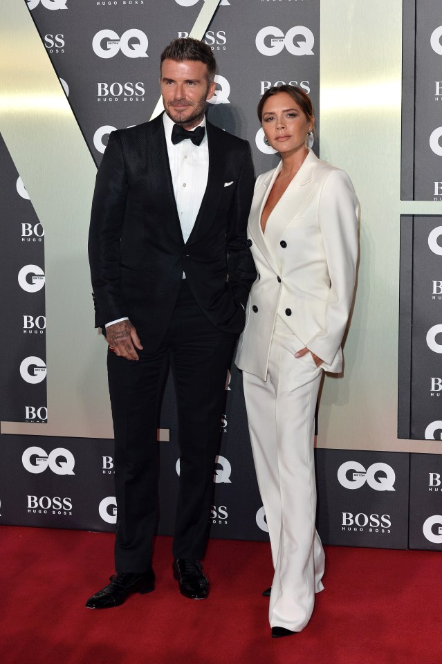 a man in a tuxedo and a woman in a white suit pose on a red carpet sponsored by boss