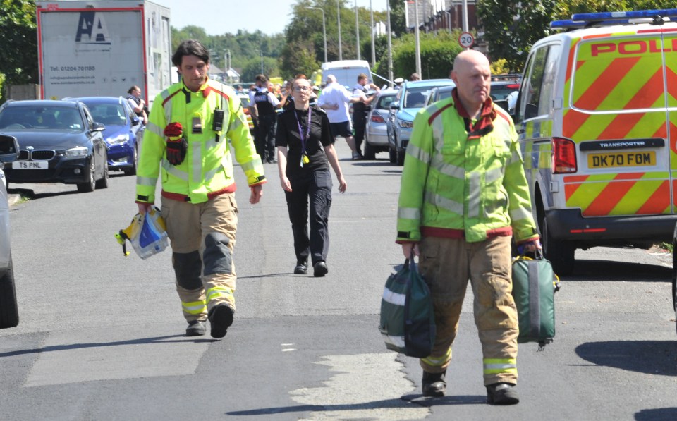 a group of firefighters walking down a street next to a police van