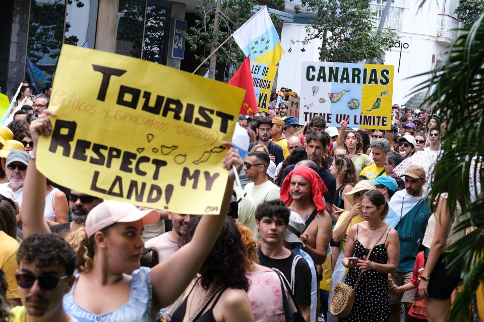 a crowd of people holding signs including one that says tourist respect my land