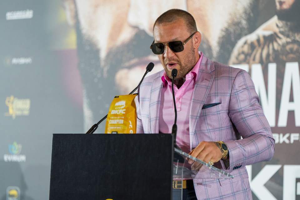 a man wearing sunglasses and a pink suit stands at a podium