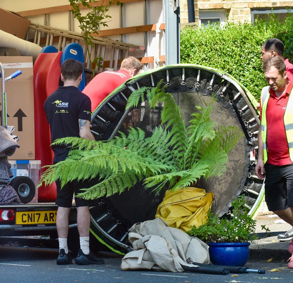 A trampoline and some plants get put into the back of the removal van