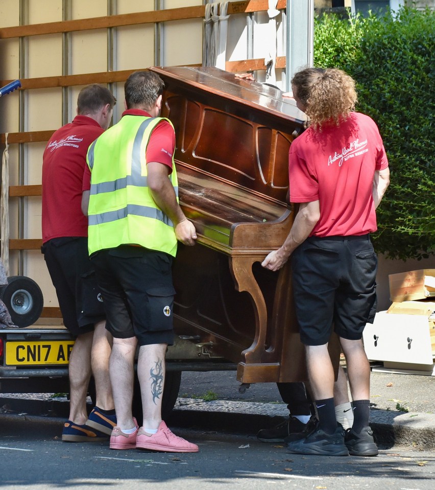 Removal men load a piano into the back of the van