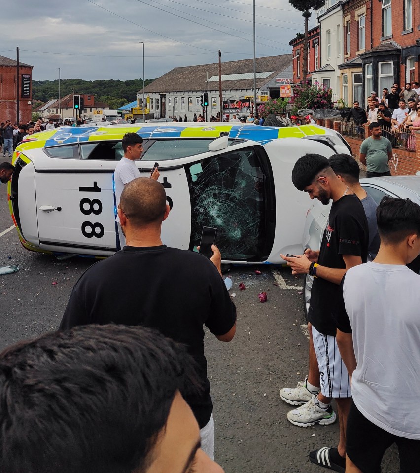 A police car was left lying on its side after being flipped over by thugs